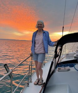 Joanne, standing on deck of a sailboat with a sunset behind her.